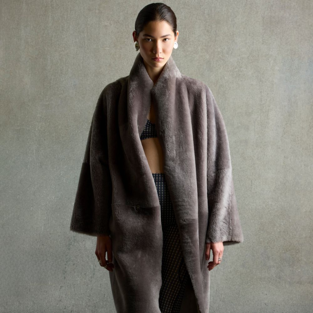 Woman wearing grey merino shearling coat by gushlow & cole on grey background