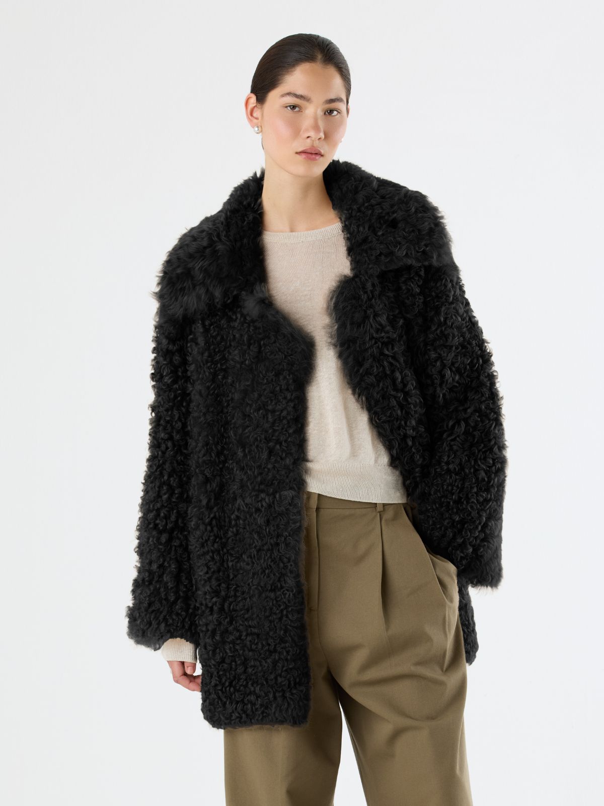 woman wearing Black Relaxed Fit Curly Shearling Coat with hand in pocket by Gushlow & Cole over green trousers