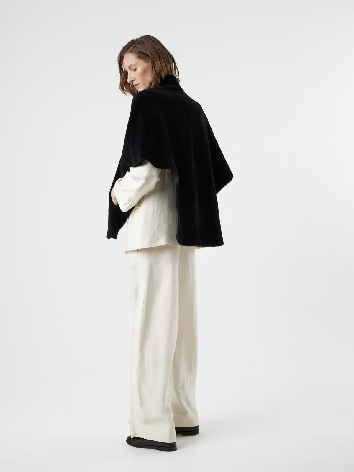 back view of woman wearing Black Shearling Cape Jacket in merino by gushlow & cole on white background