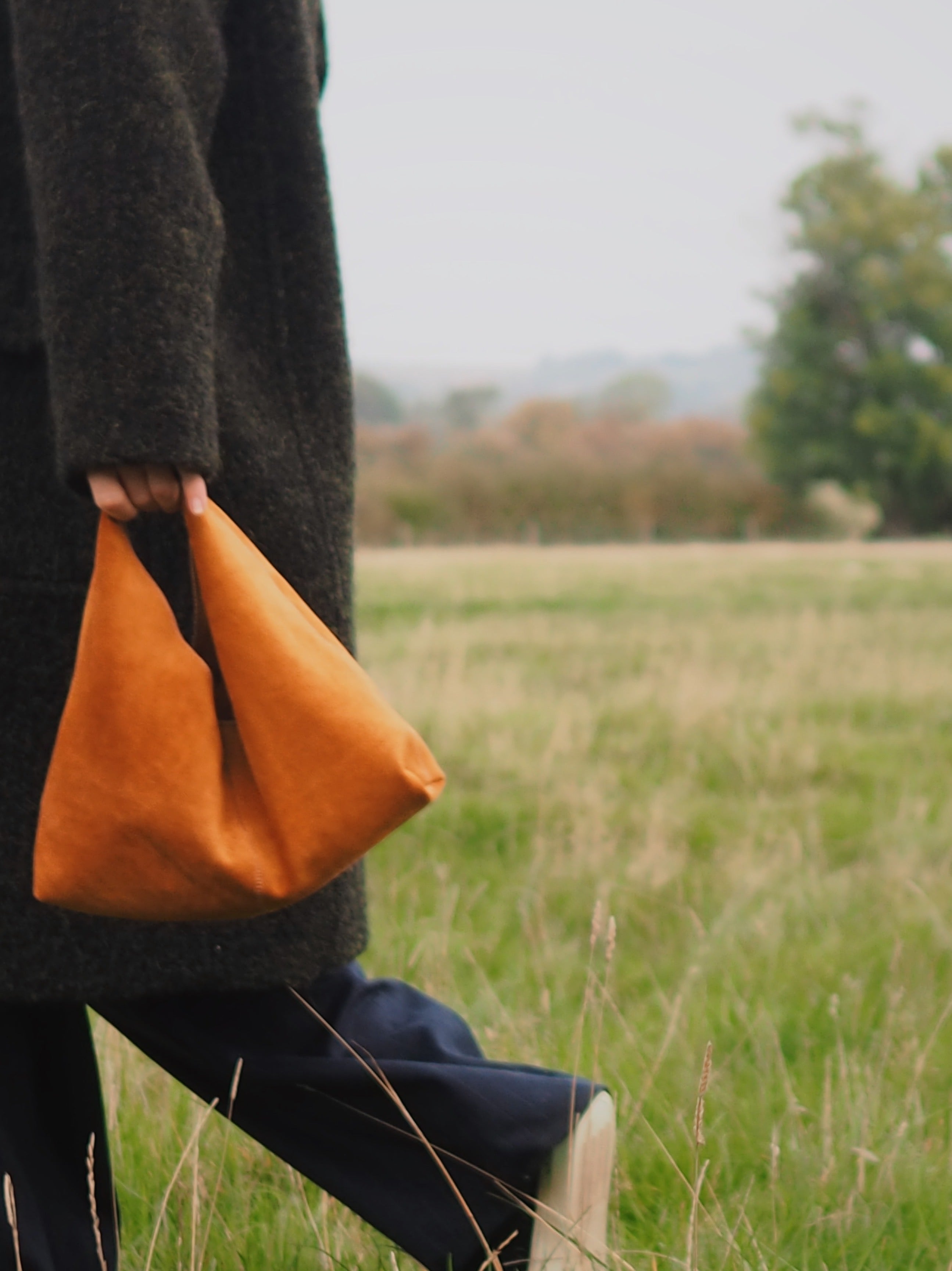 woman walking through fields with Clara Small Tan Suede Shoulder Bag by gushlow & cole