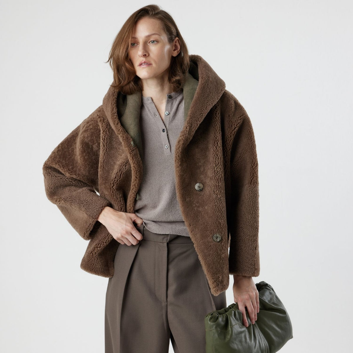 woman wearing reversible brown shearling jacket and green leather clutch bag by gushlow & cole