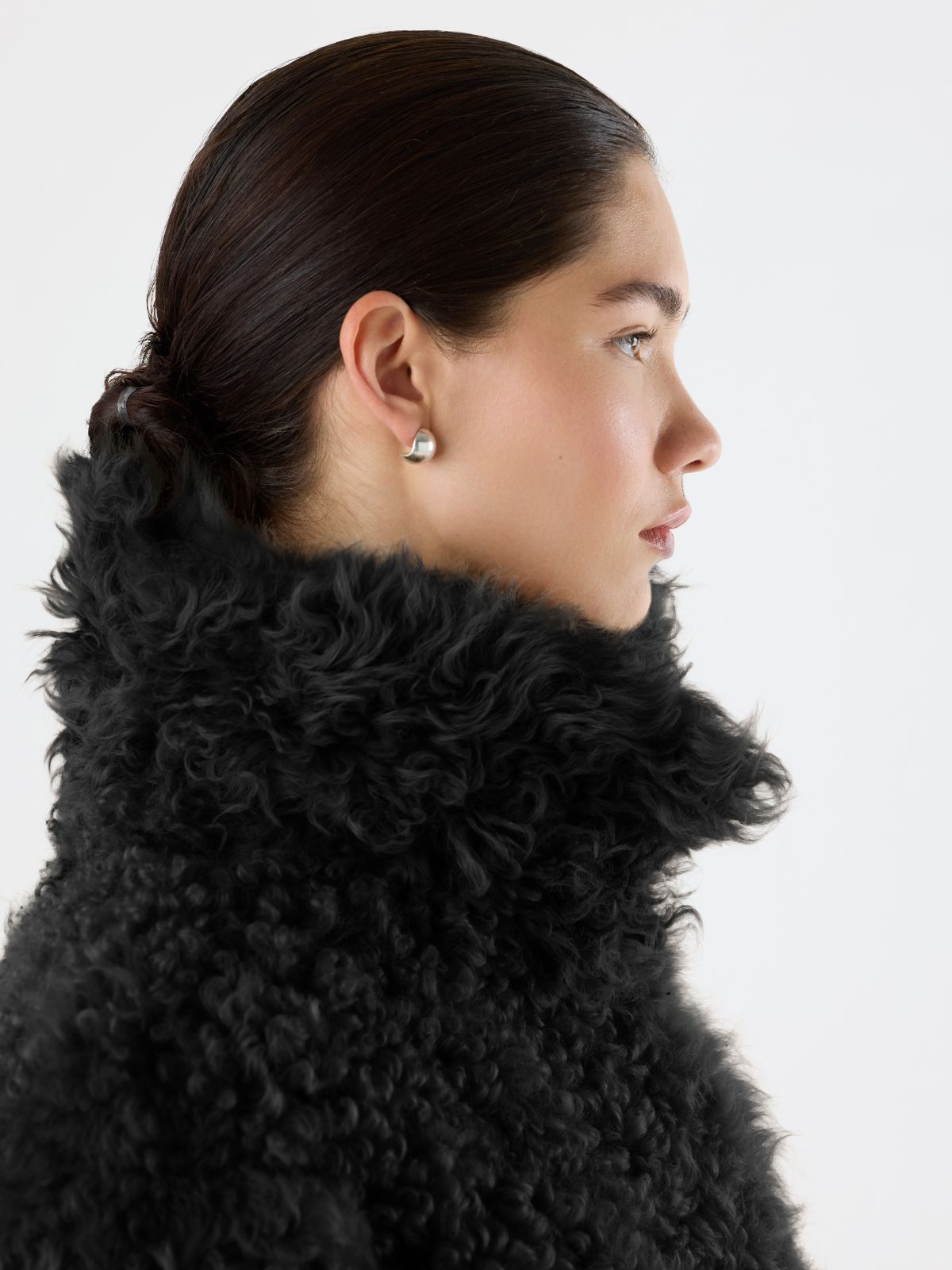 woman wearing Black Relaxed Fit Curly Shearling Coat with collar up by Gushlow & Cole over green trousers