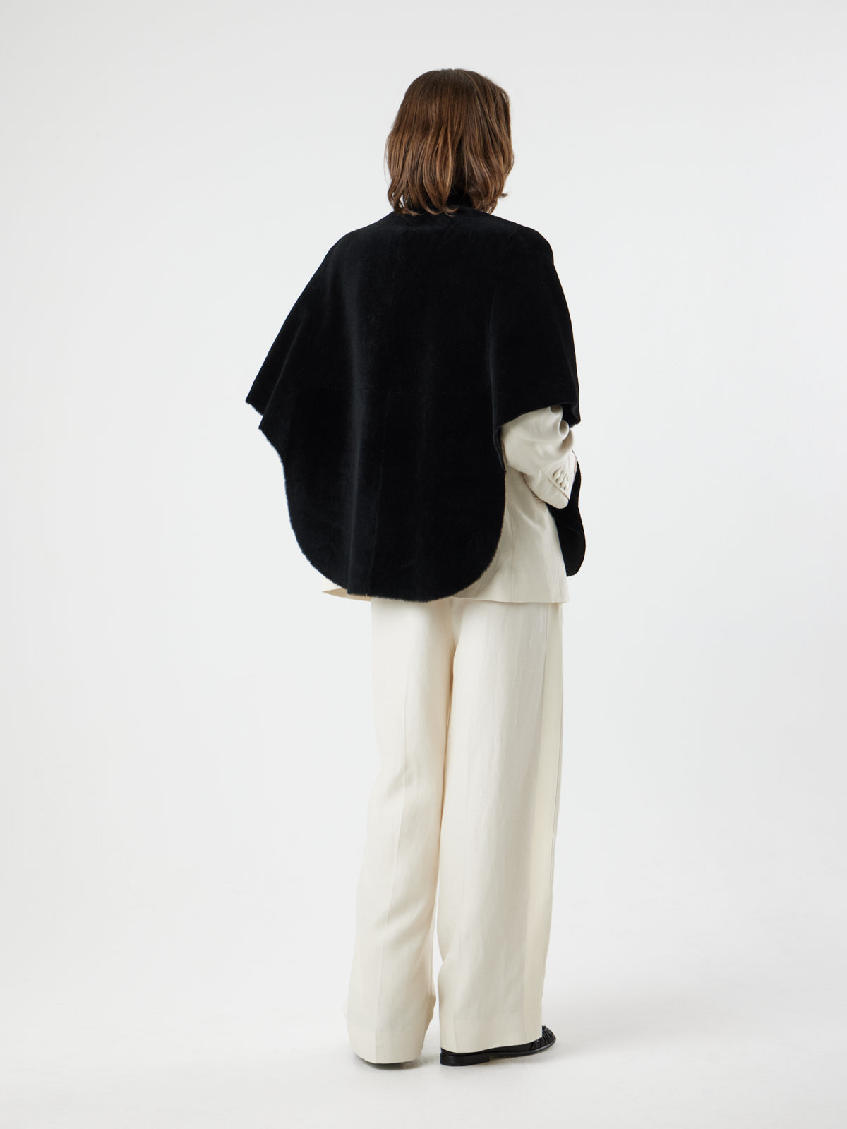 back view of woman wearing Black Shearling Cape Jacket in merino by gushlow & cole on white background