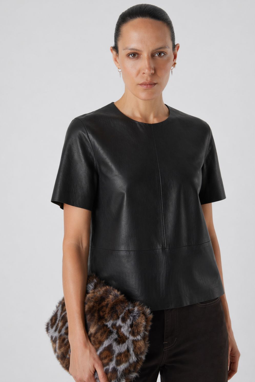 woman wearing black leather t shirt top holding shearling bag on white background by gushlow & cole