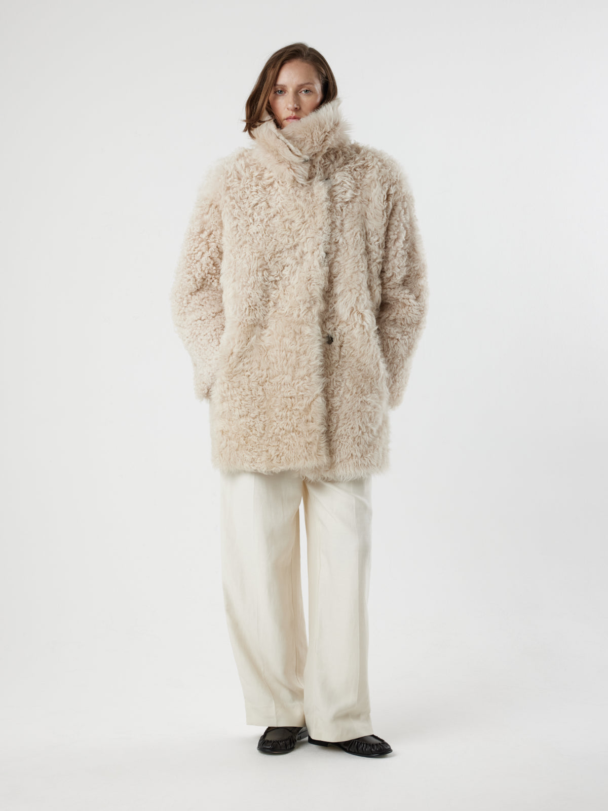 women with hands in pockets on white background wearing Cream Relaxed Fit Curly Shearling Coat by gushlow & cole 