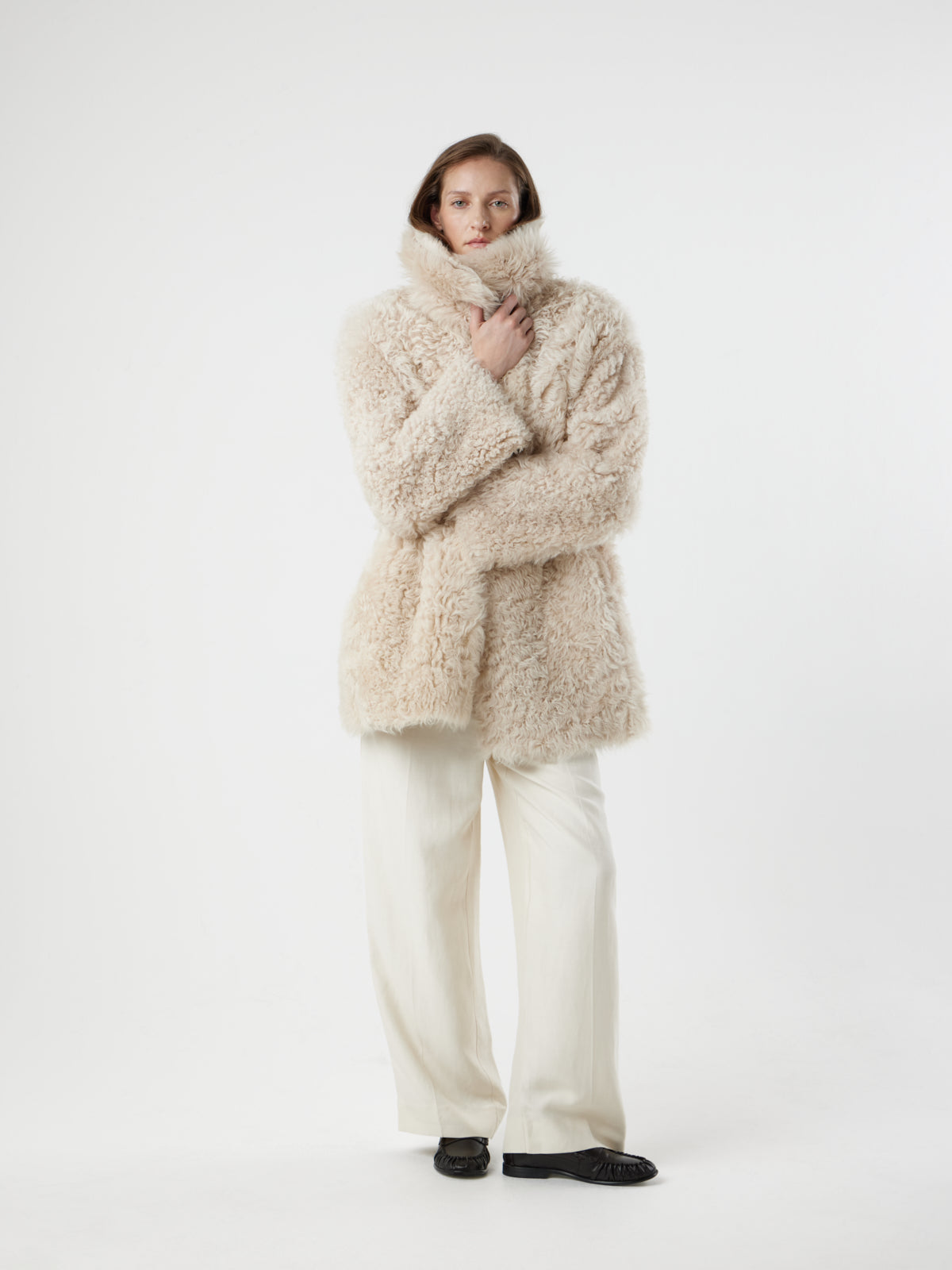 women on white background wearing Cream Relaxed Fit Curly Shearling Coat by gushlow & cole, holding collar of coat