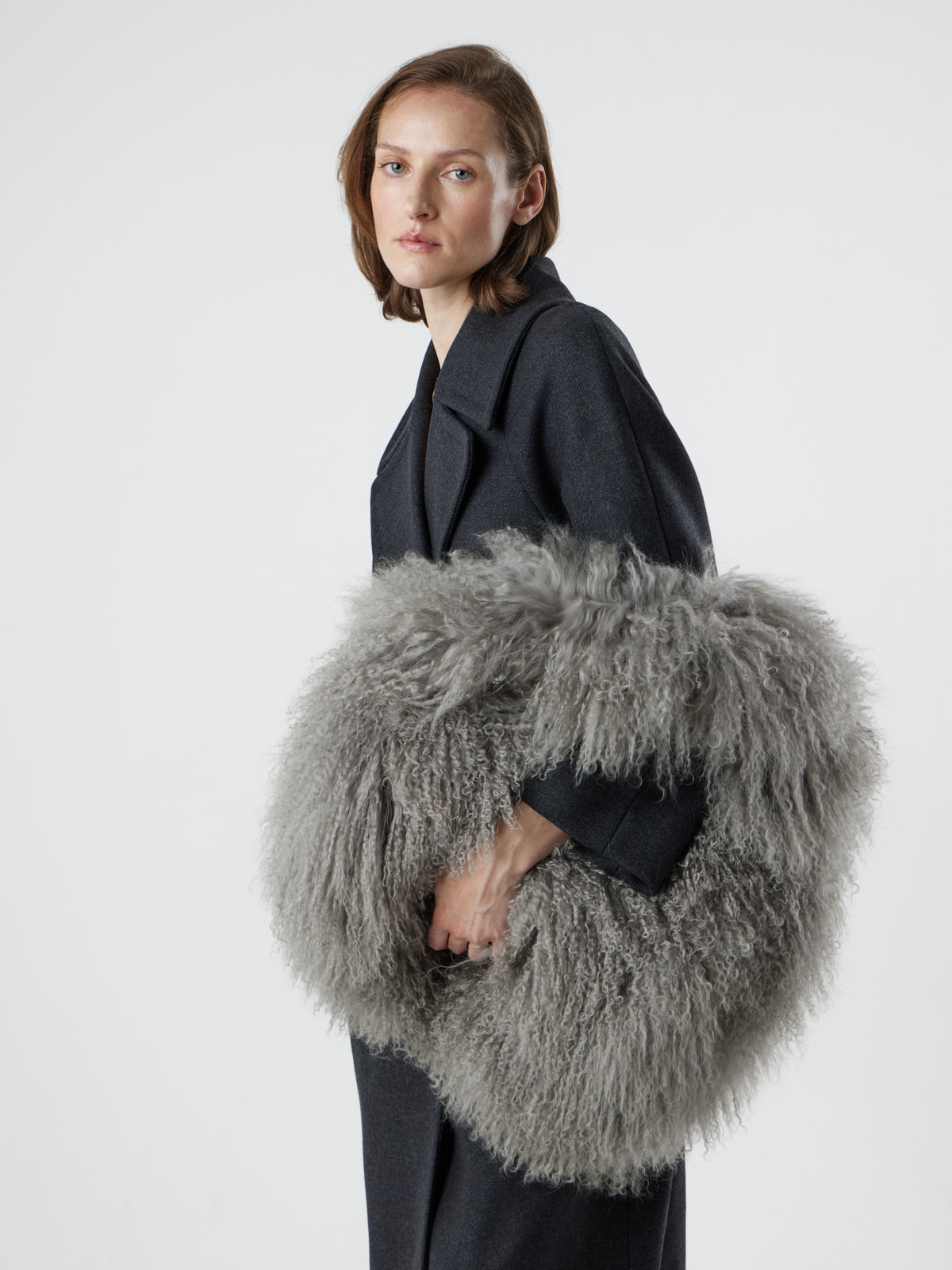 Woman holding Large Grey Mongolian Shearling Shoulder Bag over wrist by gushlow & cole on white background