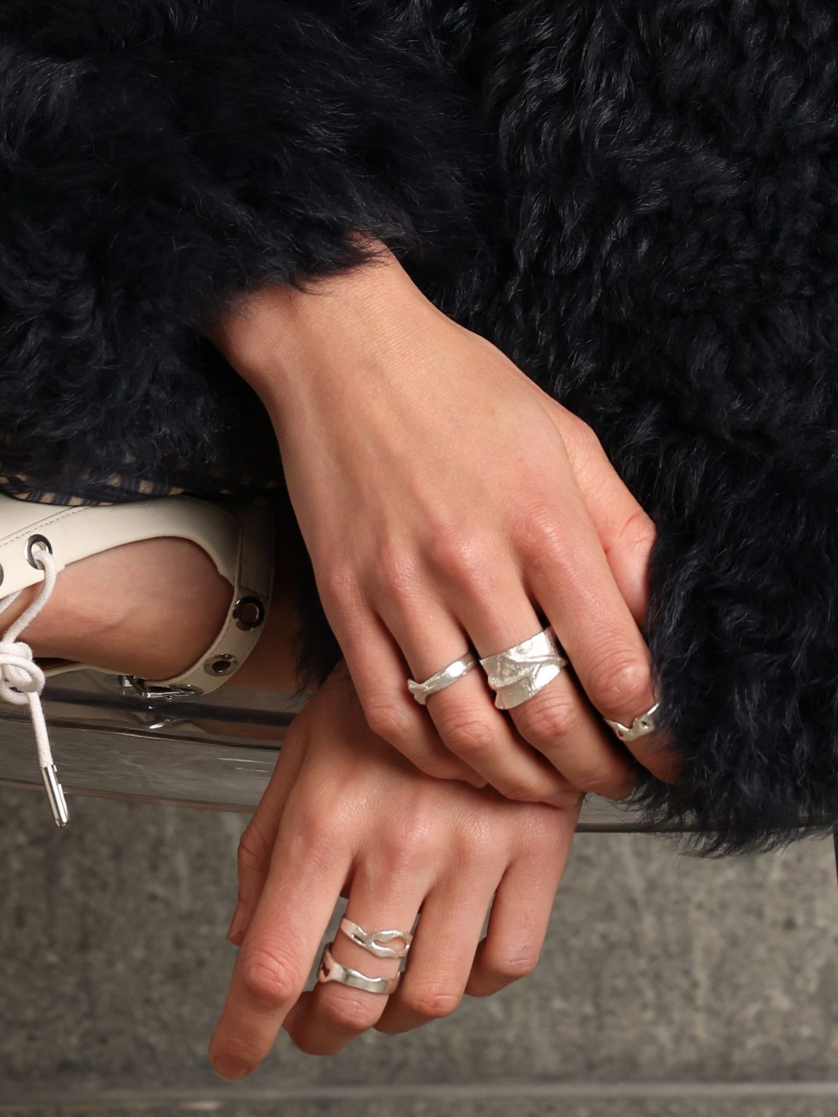 woman wearing sterling silver furrow ring by studio agaea and blue curly shearling coat by gushlow & cole on concrete background