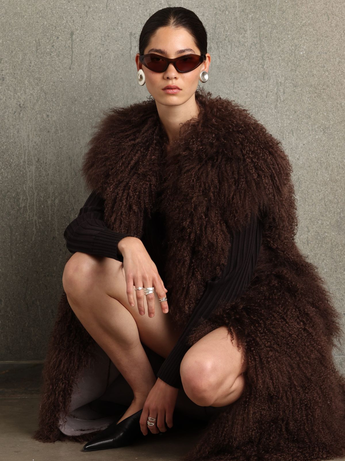 woman wearing sterling silver ripple ring by studio agaea and brown mongolian shearling gilet by gushlow & cole on concrete background