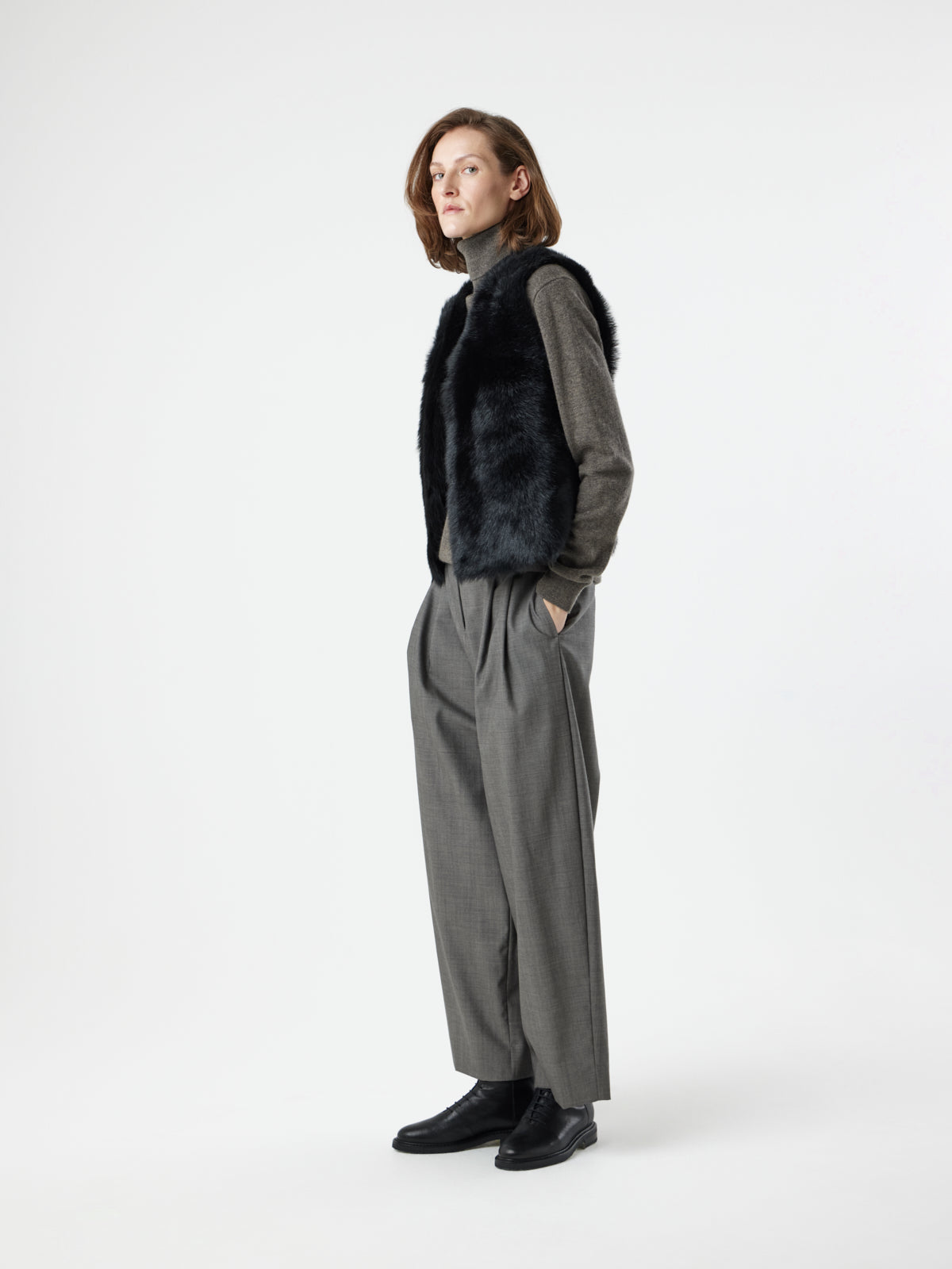 woman wearing Two Button Black Shearling Vest by gushlow & cole with hands in pockets, on white background 