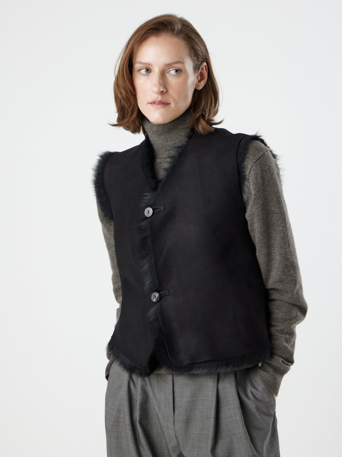 woman wearing reversed Two Button Black Shearling Vest by gushlow & cole with hands in pockets, on white background 