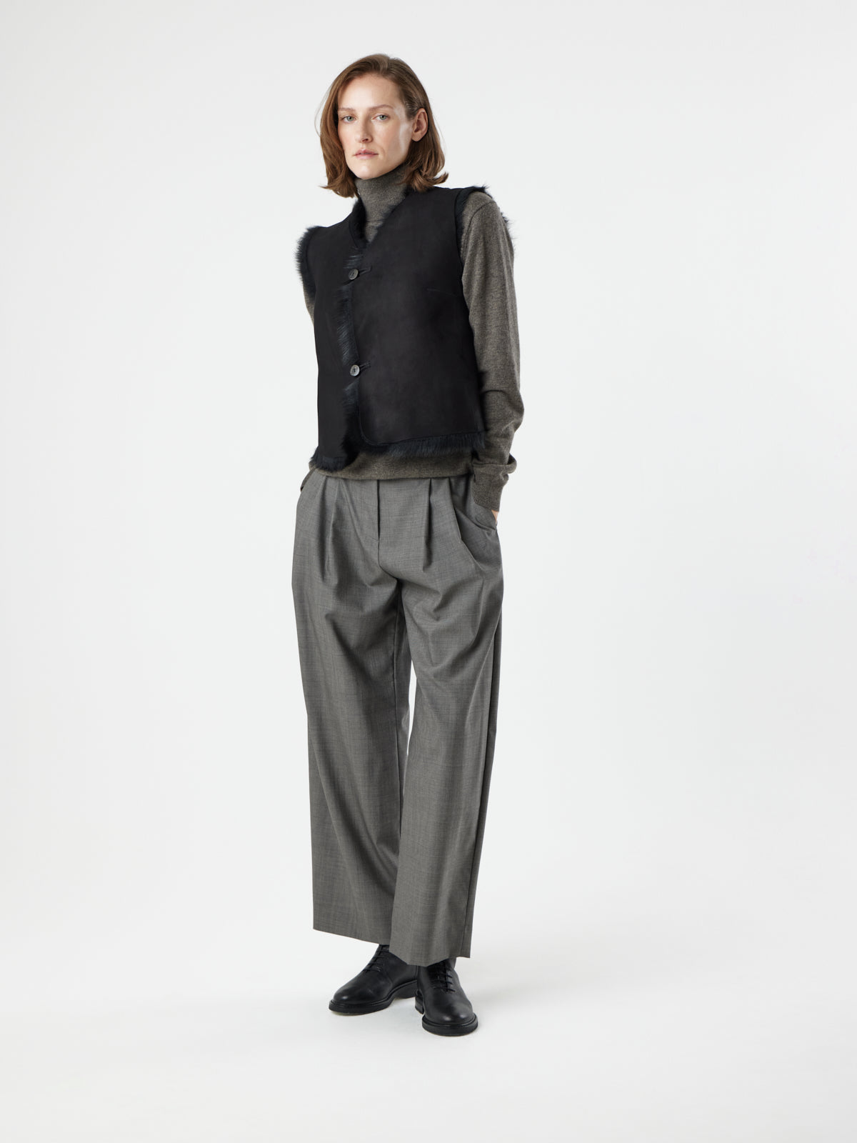 woman wearing reversed Two Button Black Shearling Vest by gushlow & cole with hands in pockets, on white background 