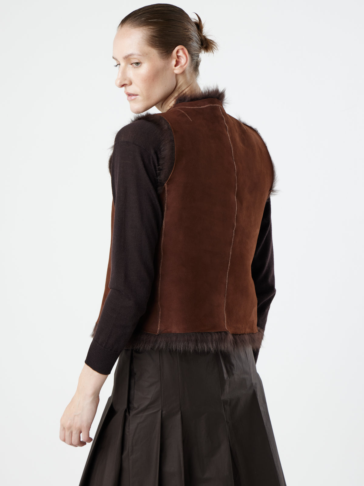 back view of woman wearing reversed Two Button Brown Shearling Vest by Gushlow & Cole over brown jumper on white background