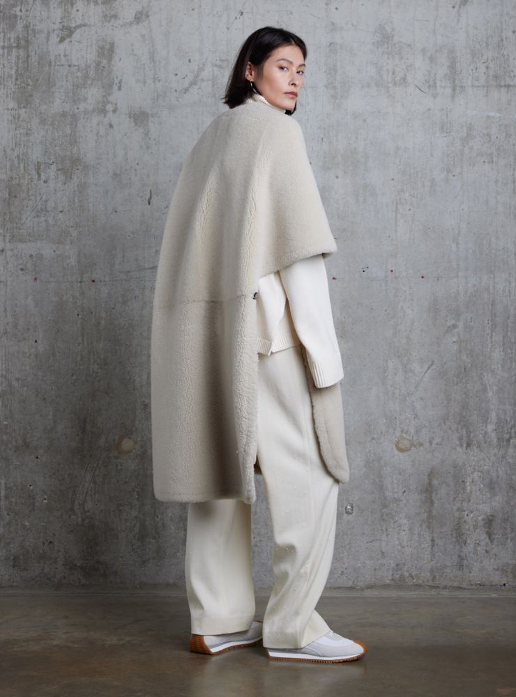 woman wearing long shearling cape on grey concrete background - luxury womens shearling gushlow & cole - our materials 