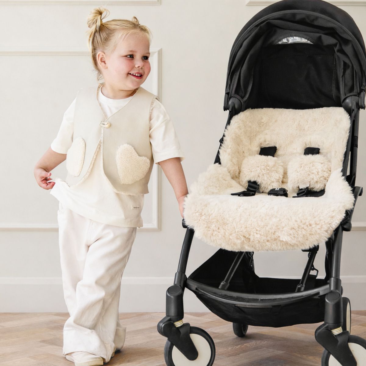 child wearing white shearling gilet by gushlow & cole standing next to cream shearling pram liner